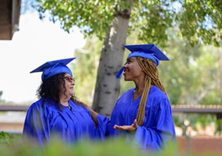 two female graduates smiling at each other during a commencement ceremony