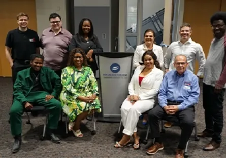 Eleven attendees of the small business networking event pose together for a group photo in front of a Rio Salado College podium. They are dressed in a mix of business and casual attire, smiling warmly at the camera in a spacious event room with wood-paneled doors in the background.