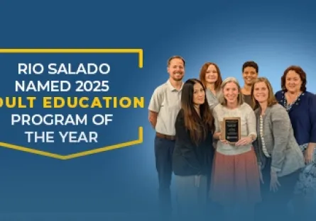 A group of Rio Salado College staff members stand together smiling, with one person in the center holding a plaque. The background features a blue gradient with white and yellow text that reads: “Rio Salado Named 2025 Adult Education Program of the Year.” The team poses proudly, representing the college’s award-winning adult education program.