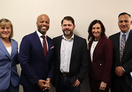 Five leaders stand side by side against a light-colored wall. From left to right: Rio Salado College President Kate Smith in a light blue suit; City of Tempe Mayor Corey Woods in a navy suit with a red tie; Arizona Sen. Ruben Gallego in a dark blazer and open-collar shirt; Tempe Chamber President & CEO Robin Arredondo-Savage in a burgundy suit; and MCCCD Chancellor Steven Gonzales in a dark suit with a patterned tie. All are smiling and facing the camera.