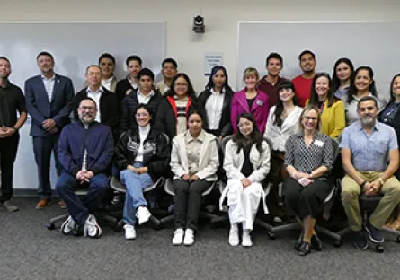 Group photo of students and instructors gathered in a classroom, standing and seated in rows.