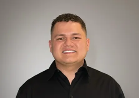Portrait of Yeison Ramirez Mendez smiling in a black button-up shirt against a gray background.