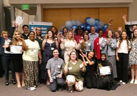 Group photo of approximately 20 Rio Salado College educator preparation program completers and staff posing indoors in front of blue and white balloons. Several individuals are holding certificates, and banners for the Educator Preparation Program are visible in the background. Participants are arranged in rows, smiling and facing the camera during a recognition event.