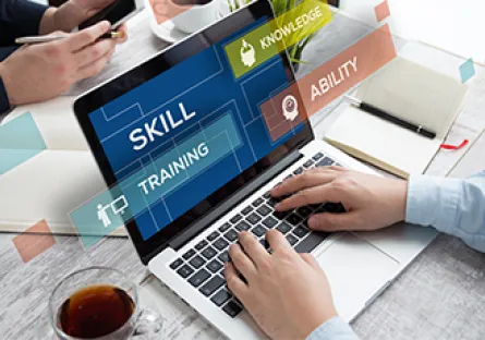 Person typing on a laptop at a desk with a phone, notebook, and coffee nearby, with overlay text reading “Skill Training,” “Knowledge,” and “Ability.”