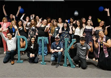 Large group of newly inducted Phi Theta Kappa members posing together on stage behind large “PTK” letters during the 2026 induction ceremony.