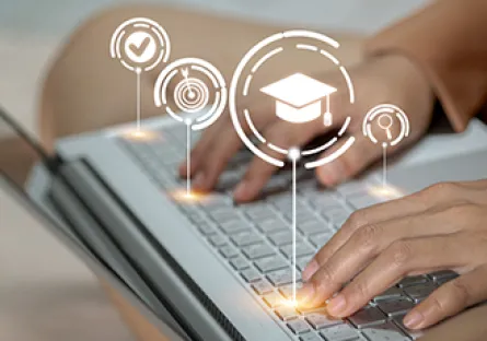Hands typing on a laptop keyboard with digital education icons, including a graduation cap, target, checkmark, and magnifying glass, displayed above the screen.