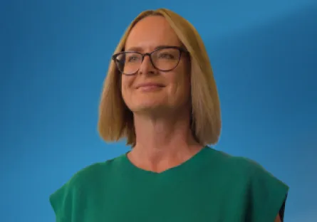 Alt text: Amy Gentry smiles while wearing glasses and a green top, posed against a blue background.