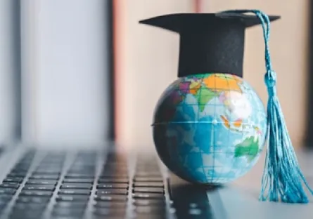 A globe next to a keyboard wearing a graduation cap