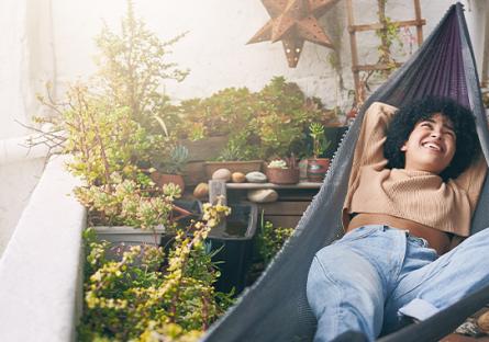 woman in a hammock on a balcony, surrounded by plants, taking a break