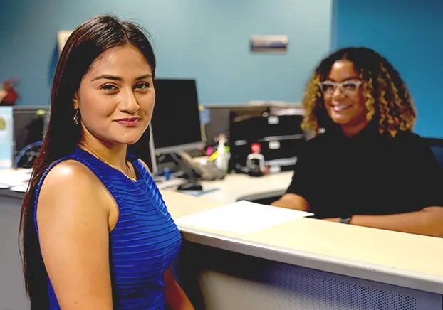 two females smiling and sitting in front of desk
